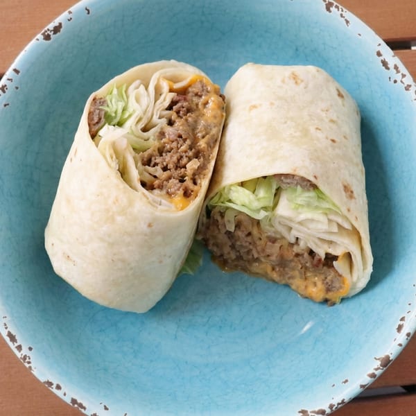 Two beef and cheese burritos with shredded lettuce, served on a distressed blue plate.