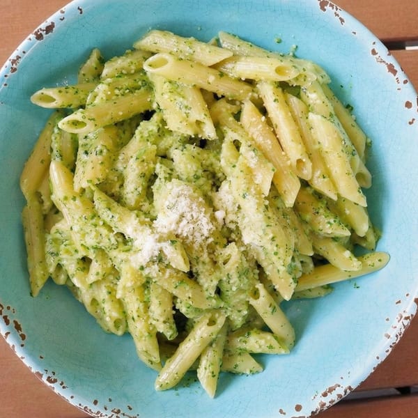 Penne pasta with green pesto sauce and grated cheese in a rustic blue bowl.