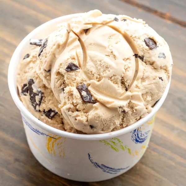 Three scoops of chocolate chip ice cream in a white cup with colorful brushstrokes on a wooden table.