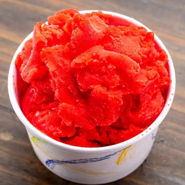 Close-up of a white cup filled with bright red Italian ice, showing its icy texture.