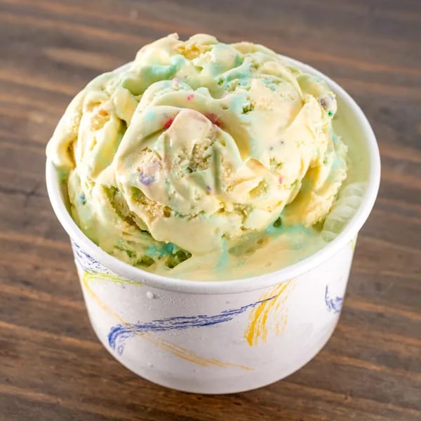 Scoops of colorful ice cream with sprinkles in a white cup on a wooden surface.