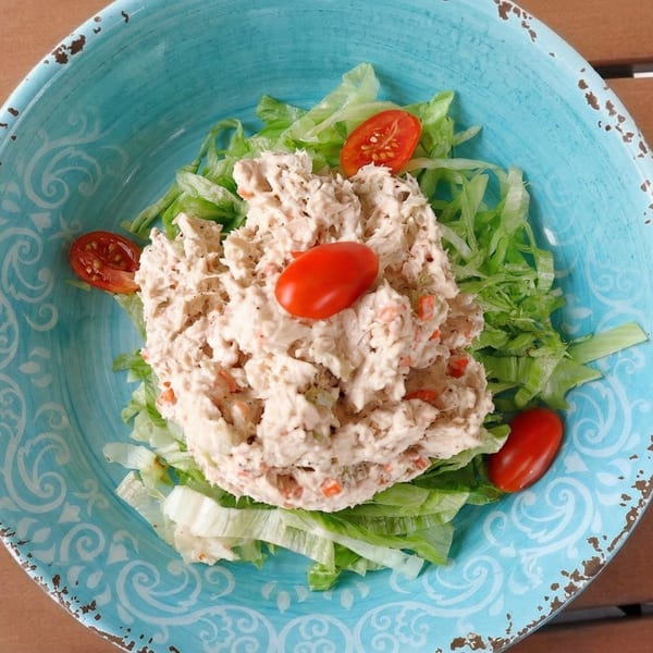 Tuna salad with lettuce and grape tomatoes in a distressed blue bowl on a wooden table.