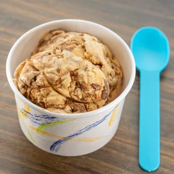 A cup of brown ice cream with chocolate chunks sits next to a bright blue spoon.